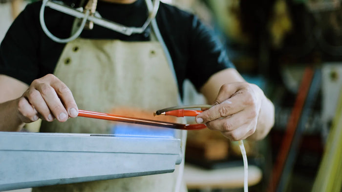 A glassblower bending a real neon glass tube over a flame by hand in the workshop