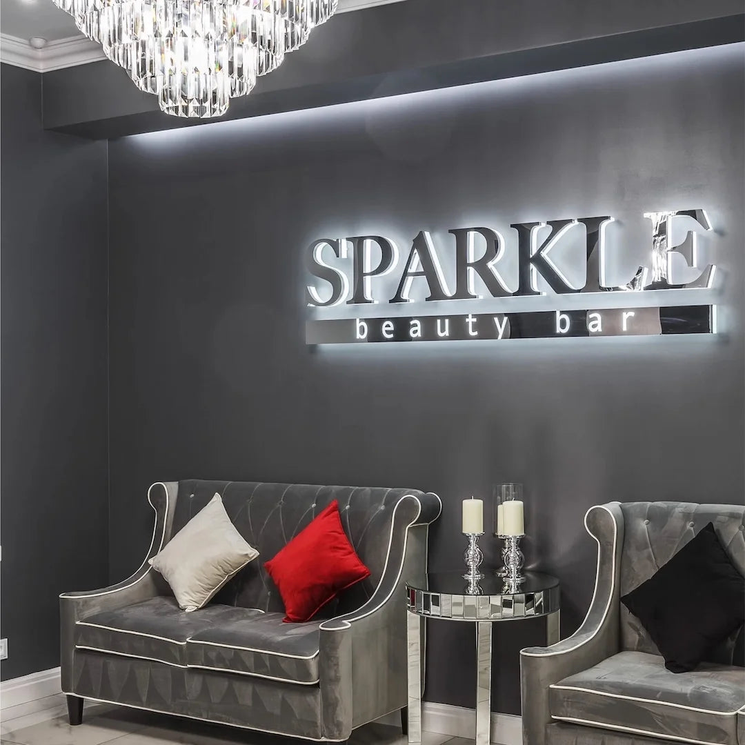 Custom halo backlit acrylic letter sign for Sparkle Beauty Bar with white glow on a dark salon wall