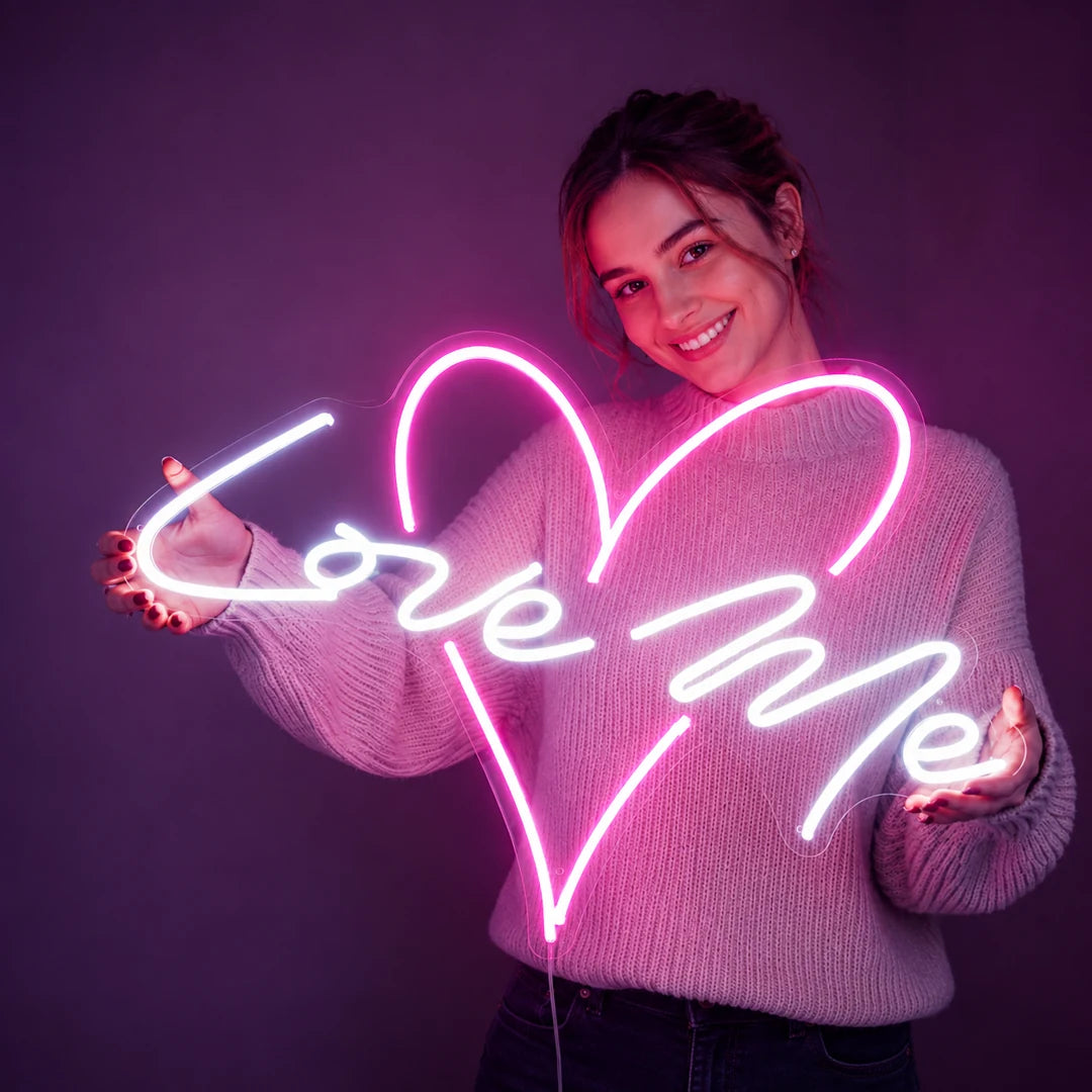 Custom LED neon Love Me heart sign — a smiling woman holding a glowing pink neon heart on a purple background