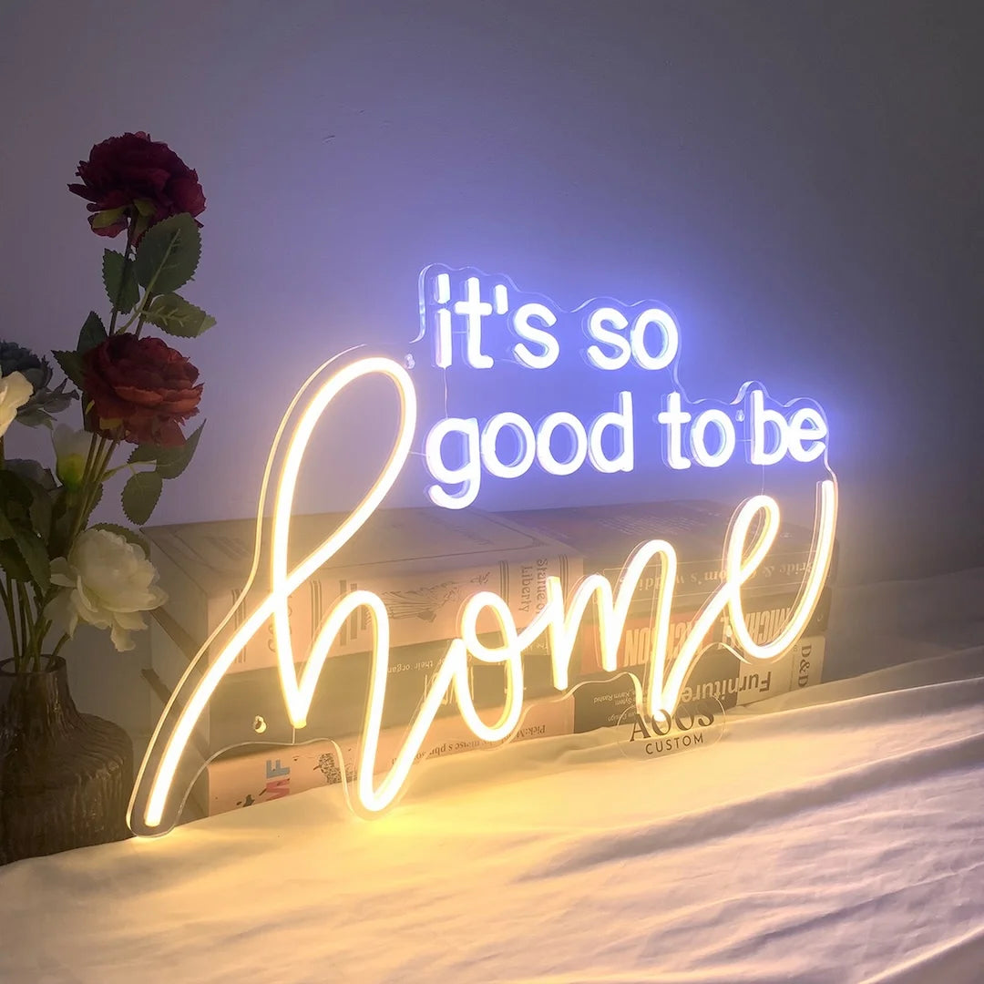 Custom battery operated LED neon sign with “it’s so good to be home” phrase on a clear acrylic stand for tabletop display