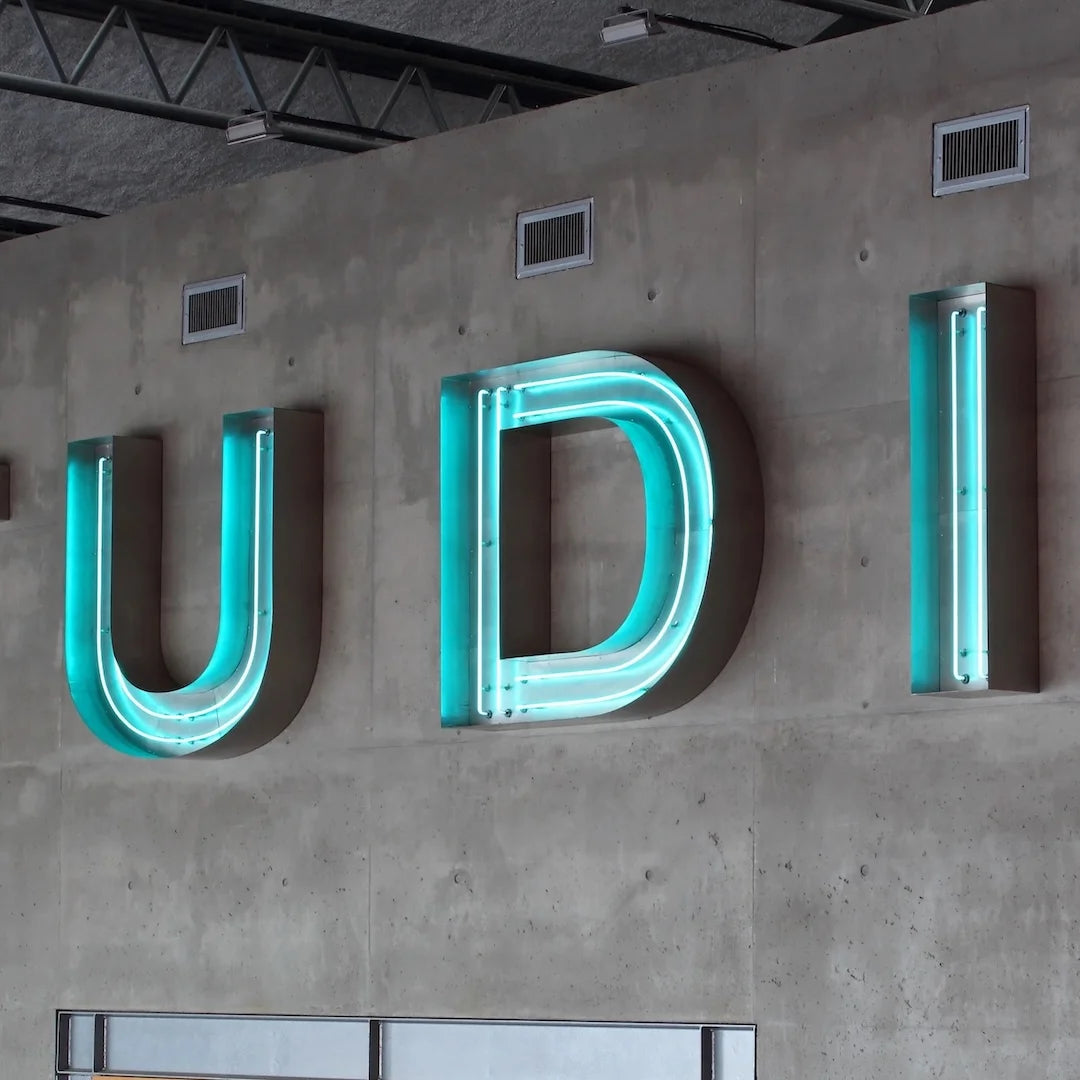 Custom open-face glass neon channel letters with three dimensional individual letters made from metal returns and exposed real glass neon tubing on the front of each letter. The sign displays a business name, logo, or custom text in raised channel letter form mounted to a storefront facade, wall, or raceway. Each letter is fabricated as a separate unit with an open front construction that reveals the illuminated glass tubing and the dimensional depth of the letter body. The installation is suitable for exte